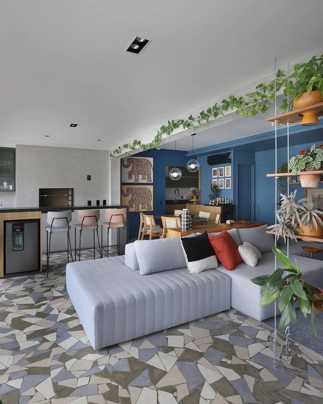 Almofadas no sofá cinza claro, piso estampado e estante azul no canto.