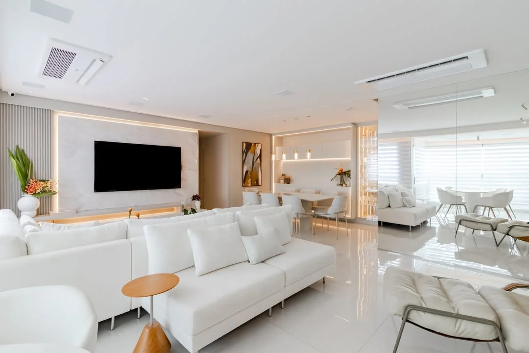 Sala de estar com sofá e almofadas brancas, parede com televisão.