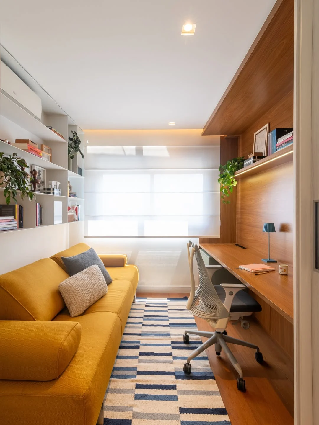 Home office com mesa de amdeira, tapete estampa geométrica e sofá amarelo mostarda.