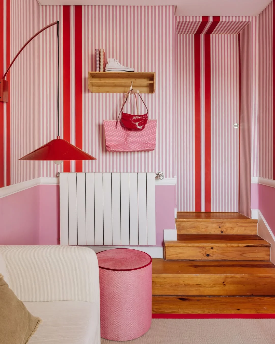 Papel de parede listrado em ambiente rosa e vermelho, escada de madeira.