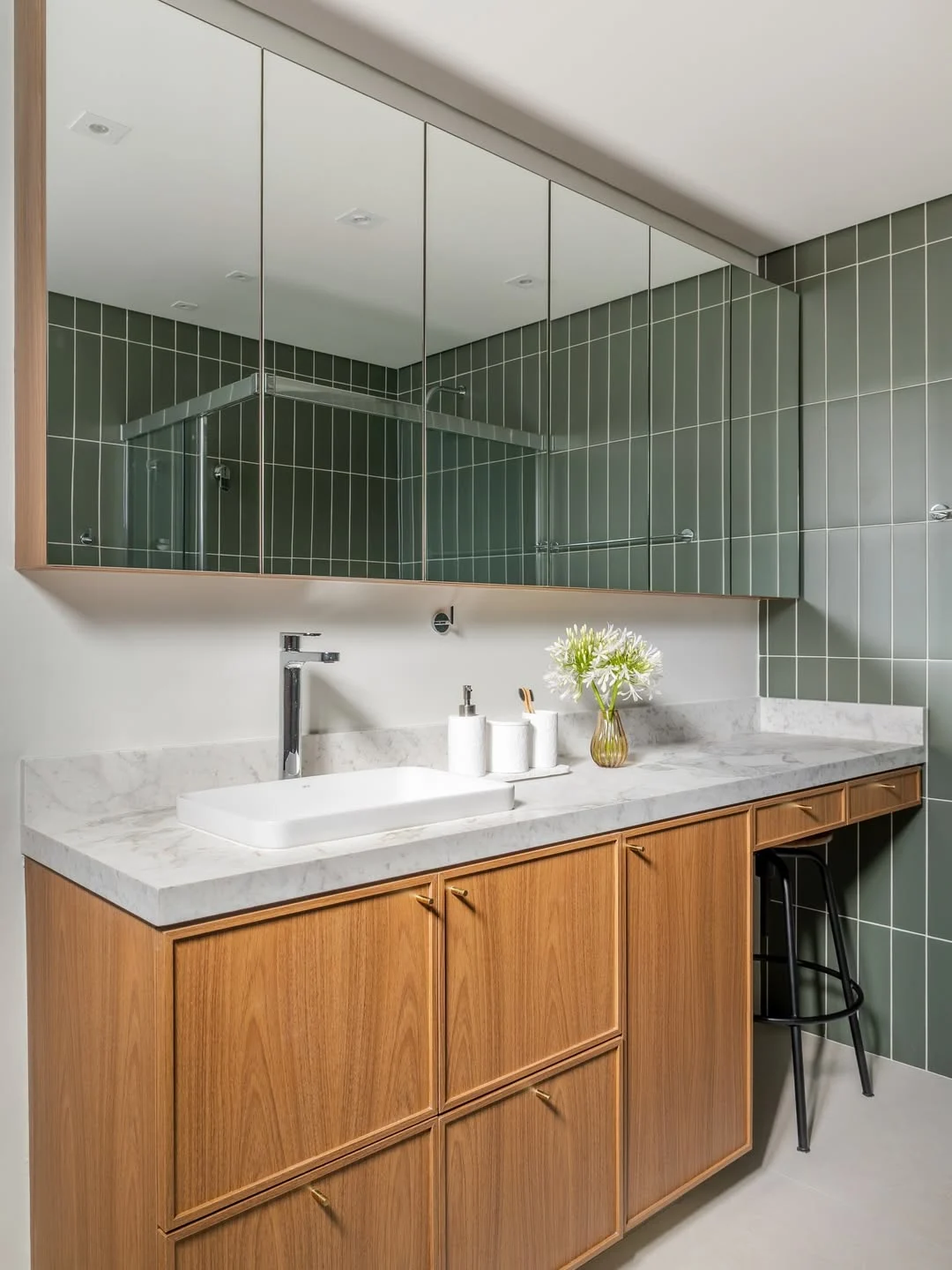 Banheiro verde com espelho grande e armário de madeira.