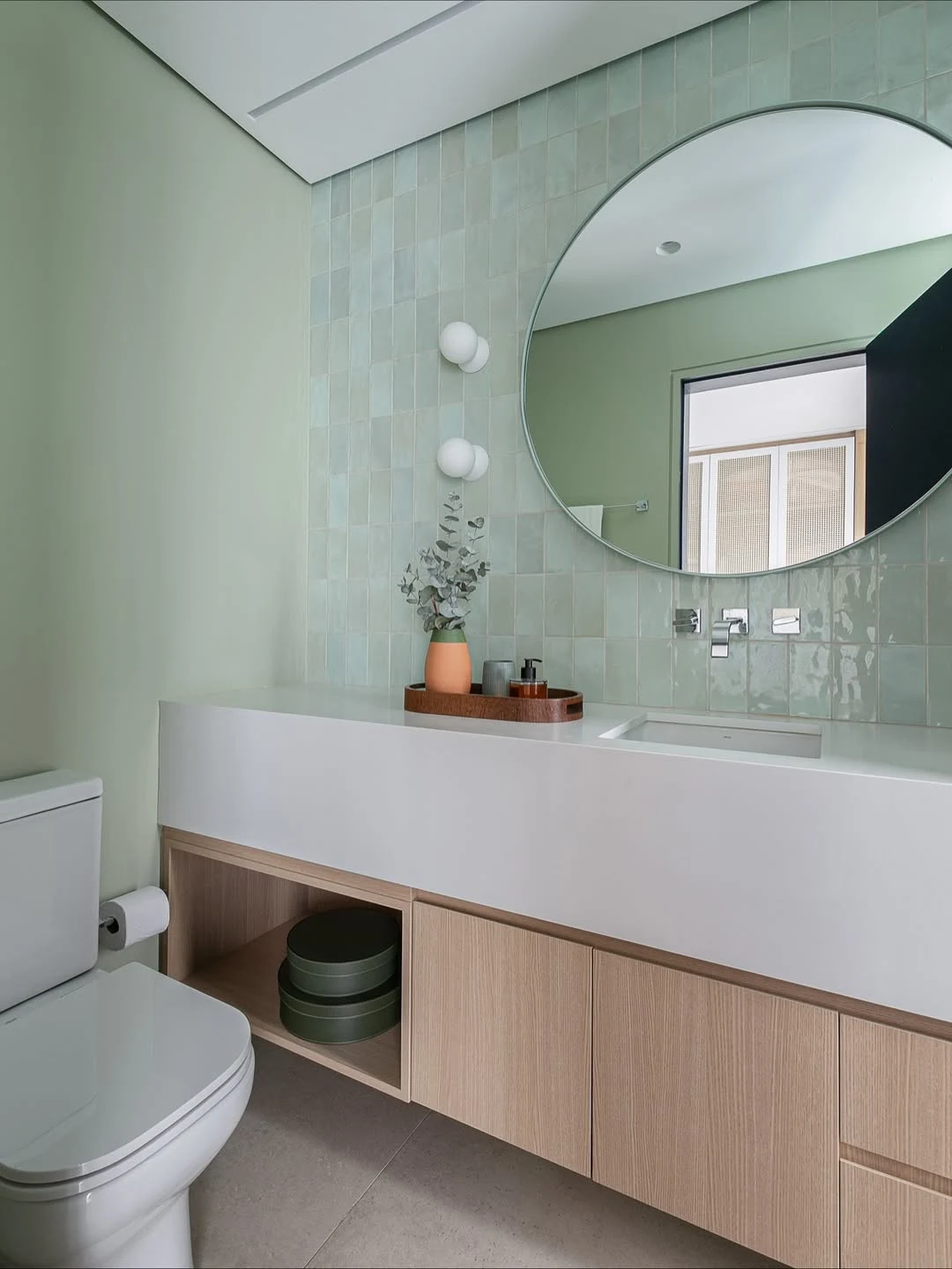 Banheiro verde claro delicado, espelho redondo.