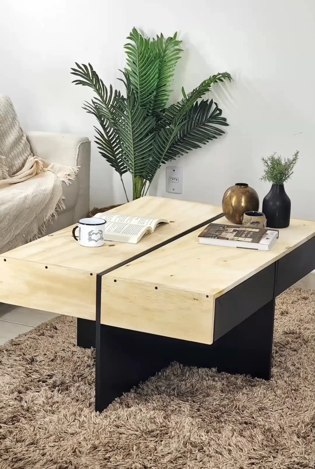 Mesa de centro com compartimento interno com tampo de madeira fechado e vasos em cima, base preta.