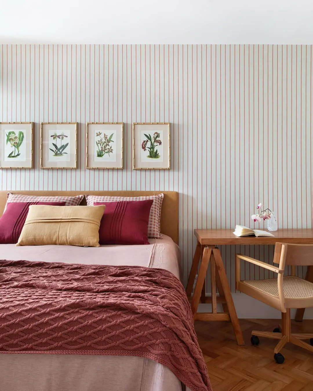 Papel de parede listrado, quadros na parede, roupa de cama rosa e vinho.