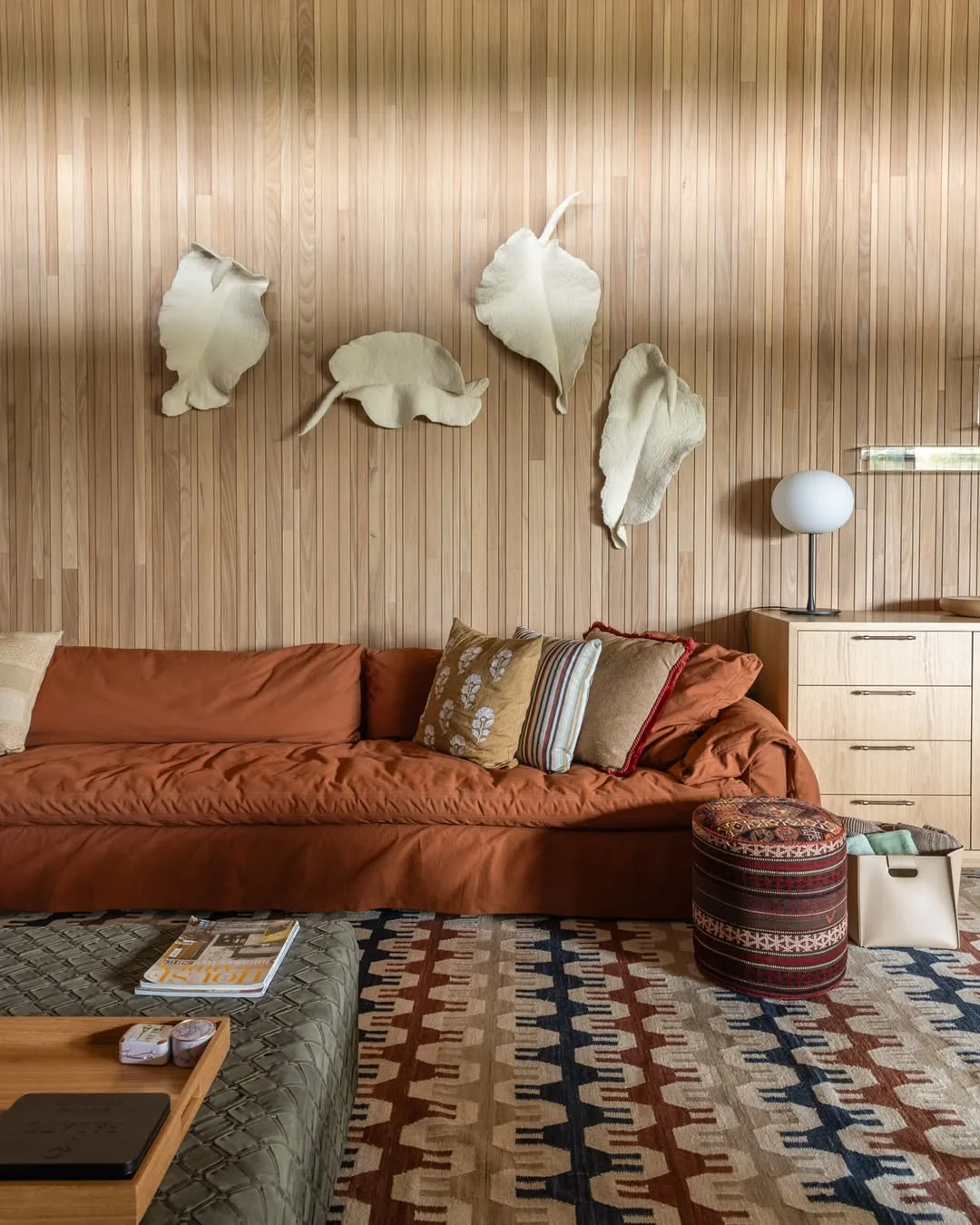 Parede de madeira com esculturas de folhas penduras, sofá terracota.